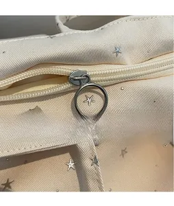 Macro detail of the smooth silver zipper and star metal hardware on a beige canvas tote bag