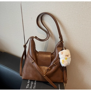 Détail du sac hobo marron vintage avec un charm ours en peluche posé sur un livre
