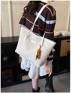 Detail of off-white leather tote bag with embossed pattern and wooden bead charm