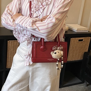 Detail of red glossy leather handbag featuring a cute plush bear charm and bead chain