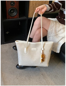 Close-up of cream tote bag with embossed pattern and wooden bead charm detail