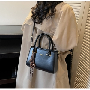 Close-up of black leather crossbody bag with gold lettering and pretzel knot charm detail