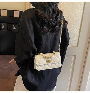 Close-up of white quilted crossbody bag with gold chain strap and metal handle detail