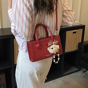 Detail of red patent leather handbag featuring a plush bear charm and metallic branding