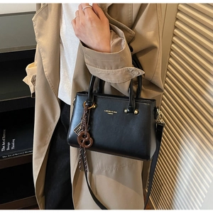 Side view of black faux leather crossbody bag with gold hardware on person in trench coat
