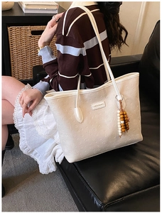 Detail of cream tote bag featuring embossed bear patterns and a stylish beaded charm