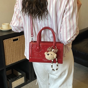 Detail of red patent leather handbag with plush bear charm and bead chain strap