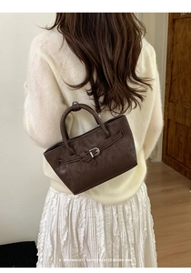 Sac bandoulière en cuir marron avec boucle argentée porté par un mannequin en intérieur