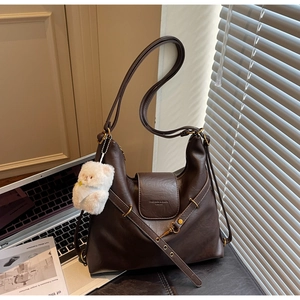 Détail du sac hobo marron vintage avec logo et charm ours en peluche sur un sac d'ordinateur