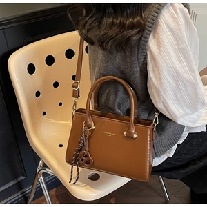 Brown leather crossbody bag detail featuring gold logo and decorative hanging charm