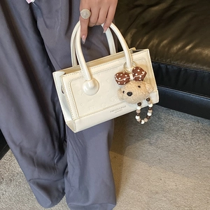 Close-up of white embossed crossbody bag with bear pendant and beaded charm