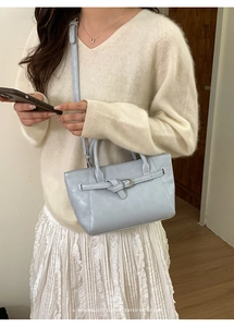 Détail d'un sac à main en cuir bleu clair avec boucle porté par un mannequin en lumière douce