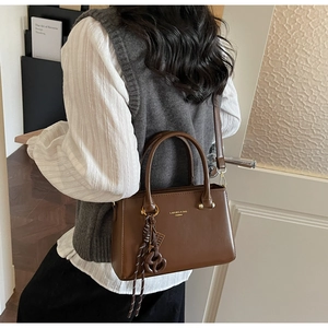 Fashionable dark brown leather crossbody bag with top handle and brand logo shown on model