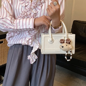 Detail of white leather handbag featuring a cute teddy bear charm and beaded strap accents