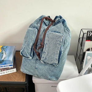 Detail of light blue washed denim backpack featuring retro drawstring and double front pockets