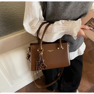 Detailed view of brown leather handbag with metallic logo and decorative woven pendant
