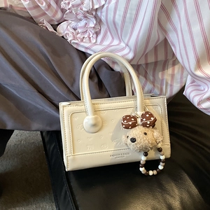 Close-up of white PU leather bag with cute puppy embossed patterns and plush charm