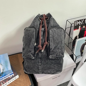 Detail of grey denim backpack featuring a drawstring closure and two front zipper pockets
