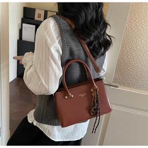 Detail of reddish-brown crossbody bag with LAIFUIKA lettering and knot pendant on model