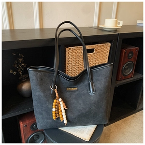 Detail of black suede tote bag with brand logo, embossed pattern and beaded tassel