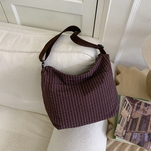 Detail view of large plaid shoulder bag with adjustable strap on white textured sofa