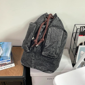 Detail of grey washed denim backpack featuring retro dual pockets and thick drawstring