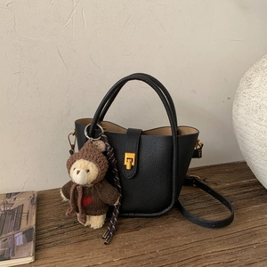 Detail van zwarte bucket bag met lychee textuur, gouden slot en een teddybeertje