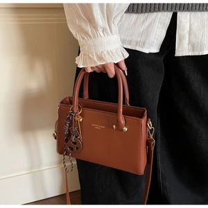 Brown leather crossbody bag detail with golden logo and decorative pendant on a model