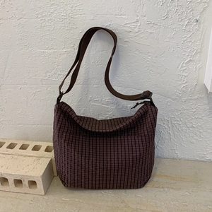 Macro detail of dark brown checkered crossbody bag with adjustable strap on stone decor