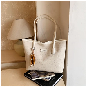 Close-up of white tote bag with embossed dog patterns and beaded charm accessory