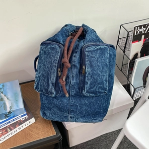 Detail of blue denim backpack showing woven drawstring and metallic zipper front pockets