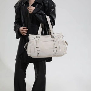 Close-up of cream tote bag with silver buckles, metal rivets and tactical strap details