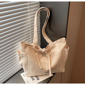 Detail of cream canvas tote bag featuring silver star prints and side pocket design