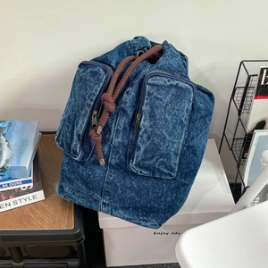 Detail of blue denim backpack with drawstring closure and dual front zipper pockets