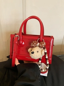 Elegant red patent leather handbag with teddy bear charm and fashion lettering detail