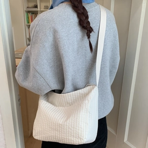 Detail of a minimalist beige plaid crossbody bag on shoulder in a cozy home setting
