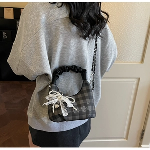 Detail of grey plaid crossbody bag featuring pearl bow charms and delicate metal chain strap