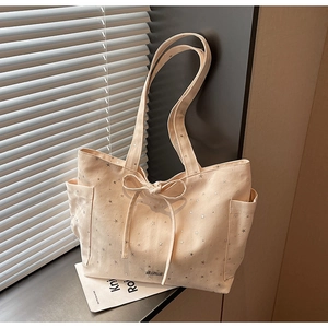 Detail of cream canvas tote bag with silver star prints and drawstring bow ornament