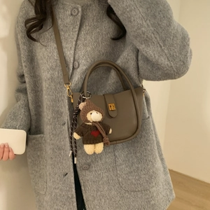Detailweergave van leren emmertas in donkere aardetint met teddybeer hanger
