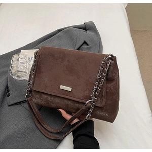 Close-up of brown vintage leather tote bag with silver brand plate and metal chain strap