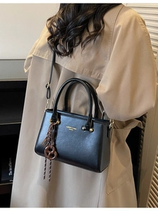 Classic black PU leather handbag with gold logo and unique woven pendant detail