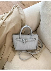 Détail d'un sac cabas en cuir gris-bleu avec sangles à boucle sur un canapé blanc