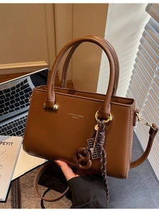 Retro brown leather handbag with adjustable strap and designer charm on a dark desk