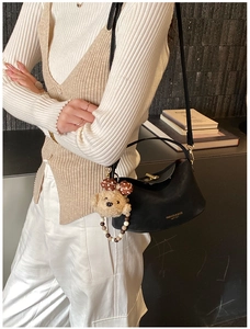 Detail of black leather handbag with metal lock and cute plush bear charm with bow