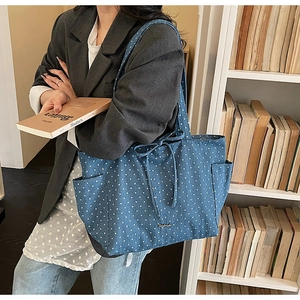Detail of blue denim tote bag with white stars, bow tie, and side pocket on a model