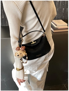 Detail of black leather handbag featuring golden lock and cute plush bear charm accessory