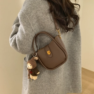 Detail van bruine leren emmer tas met gouden slot en schattige beer hanger accessoire