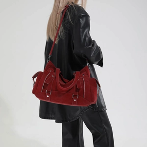 Detail of burgundy suede tote bag with silver zippers and buckle straps in studio setting