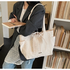 Detail of cream canvas tote bag with silver star patterns and decorative drawstring bow