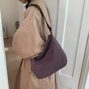 Detail of purple checkered canvas tote bag with brown fabric strap worn by a model